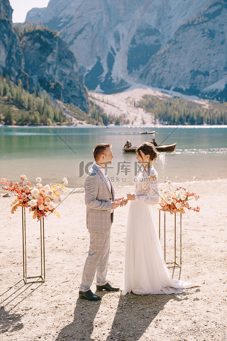 新郎在婚礼场地为新娘戴上戒指,在意大利的 Lago di Braies 背景下,以秋季花柱拱形为背景。高清摄影大图-千库网